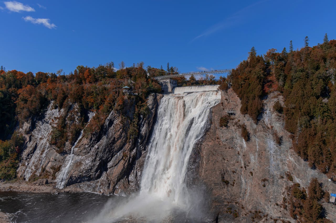 Dramatic Montmorency Falls in Québec City, Canada, surrounded by vibrant autumn foliage and clear blue skies.