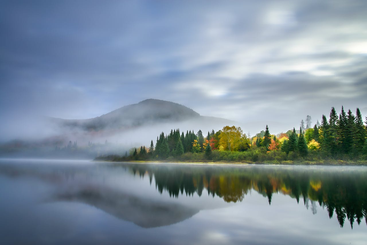 Serene view of Mont-Tremblant lake with mist, reflection, and vibrant fall foliage.